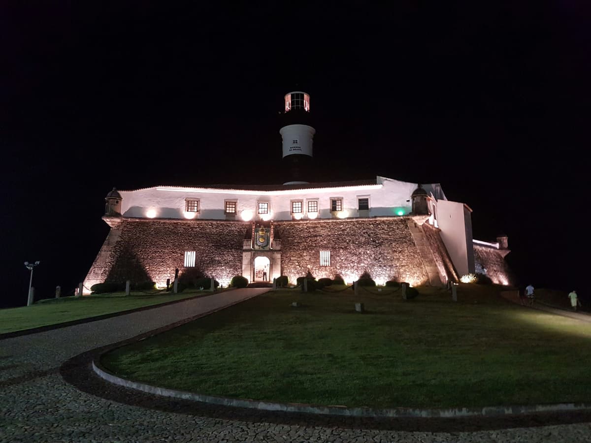 Farol da Barra illuminated at night beside the waterfront in Salvador.