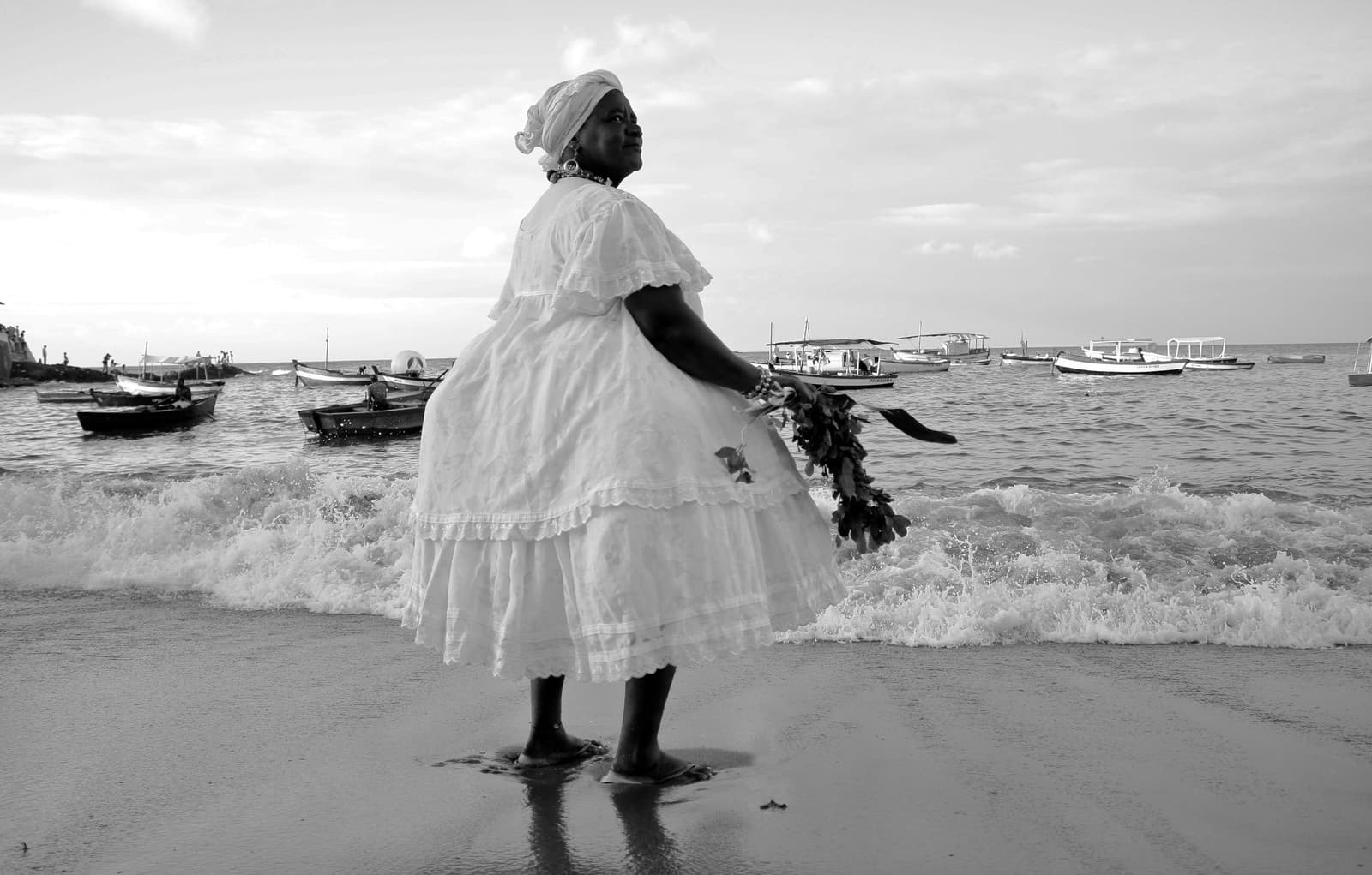 Black-and-white portrait of a mãe de santo standing by the Salvador coastline.