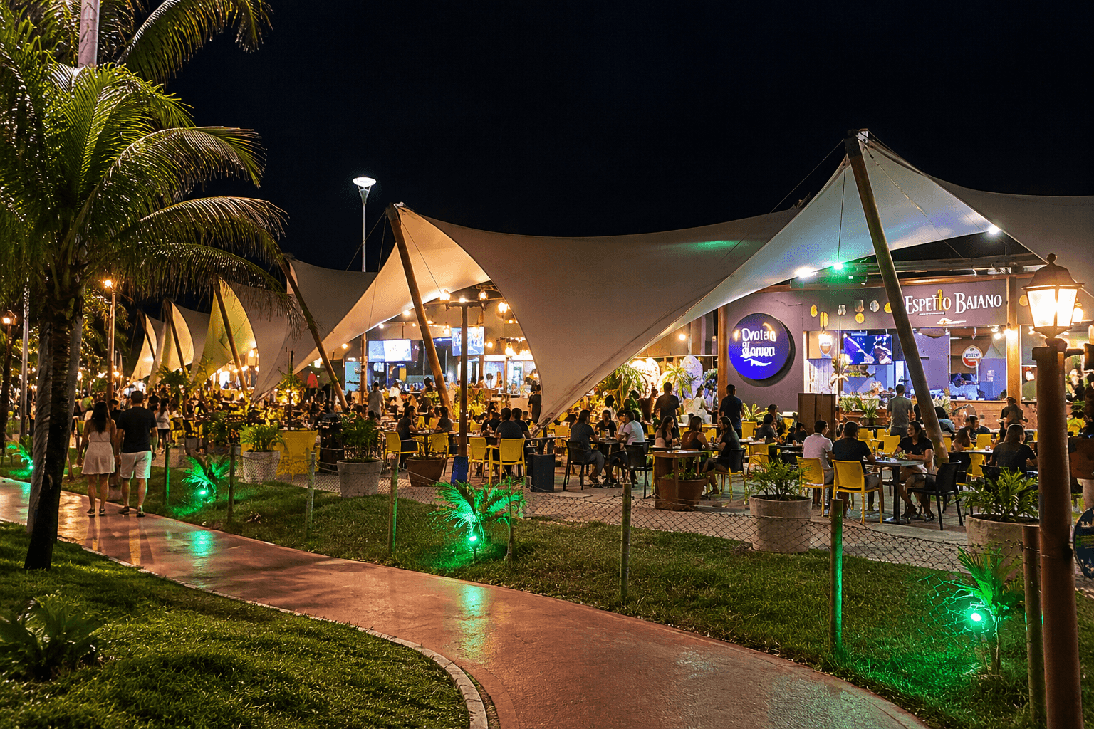 Vila Caramuru in Rio Vermelho at night, with illuminated tensile canopies, outdoor tables, tropical landscaping and people dining and walking through the complex.